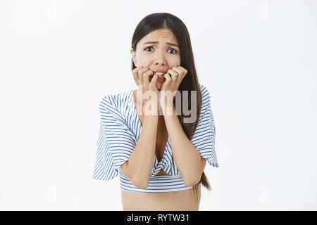 Waist-up shot of scared insecure concerned asian female in cropped blouse biting fingers and frowning shaking from fear feeling terrifying and nervous Stock Photo