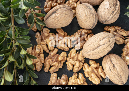 Walnut kernels near whole nuts on a dark, black background with green branches. Stock Photo