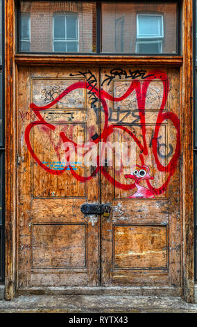 Wooden double door into a property within London's East End. Padlocked and tagged with graffiti. Stock Photo