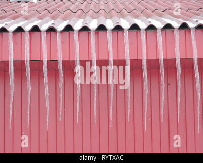 Long icicles on the red roof Springtime Stock Photo