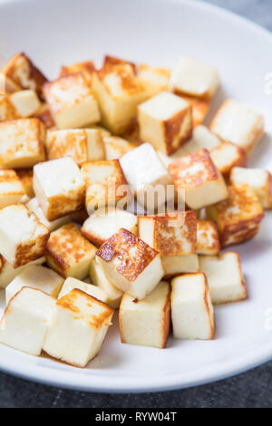 Fried small cubes of paneer in the foreground on a white plate. Close up picture of small fried cubes of cottage cheese. Pan-fried paneer cubes. Stock Photo