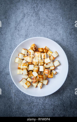 Fried paneer cubes on a white plate and grey background. Fried Indian cottage cheese on a round white plate, centered focus. Stock Photo