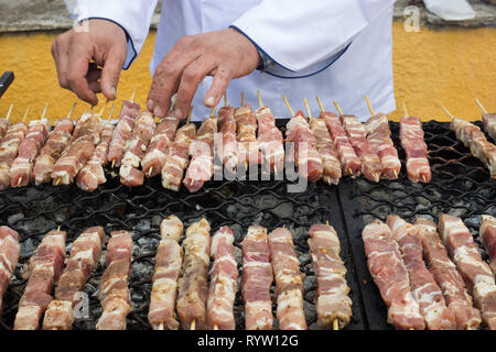 Chef hands charring Greek traditional fresh raw pork meat souvlaki cubes on wooden skewers, at the annual chestnut roasting festival. Leivadi, GR Stock Photo