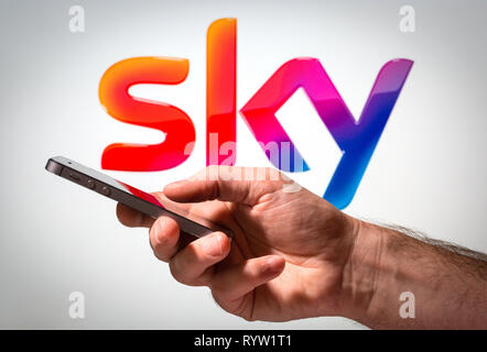 A man using a mobile phone in front of a Sky sign logo Stock Photo