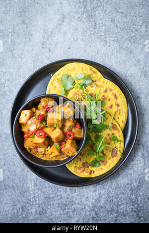 Indian malai paneer decorated with red chillies in a black bowl and 3 rotis on a black plate. Top view of Indian malai panner curry in the center and Stock Photo