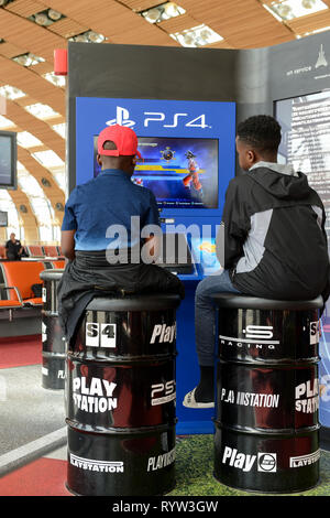 FRANCE, Paris, Charles de Gaulle airport, two african boys sitting on tin barrel and play SONY PS4 Playstation in waiting area at gates Stock Photo