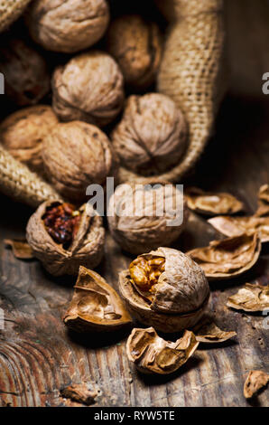 Still life with walnuts and cracked shells in vintage burlap bag. Whole walnut kernel and nutshell on rustic wooden table background. Stock Photo