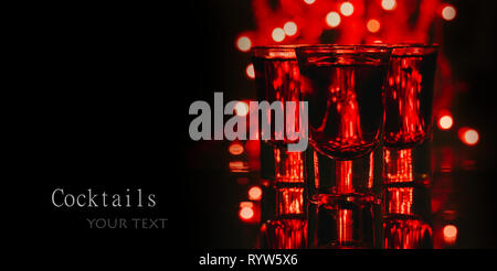 Red alcohol cocktails in shot glasses over red bokeh light and black background. Shots on bar counter in night club party. Stock Photo