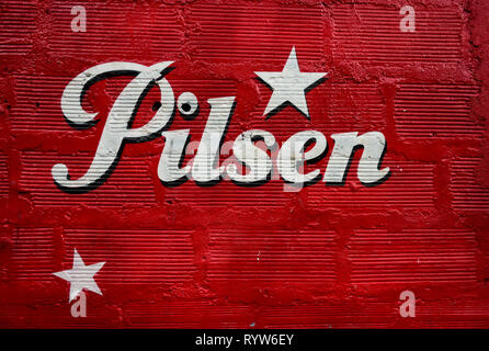 Textured red painted wall with the Pilsen beer logo,brewed since 1909, it is the leading brand in the Antioquia region of Colombia, South America. Stock Photo