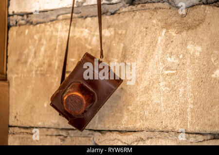 Vintage rangefinder camera in a dark brown leather case hanging from a concrete wall isolated Stock Photo