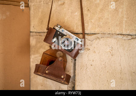 Vintage rangefinder camera in a dark brown leather case hanging from a concrete wall isolated Stock Photo