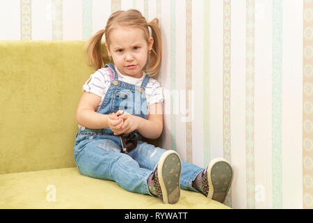 portrait of a little beautiful girl in overalls sitting on the sofa Stock Photo