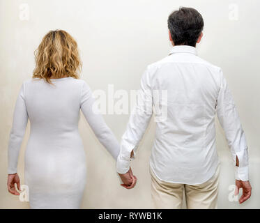 Mature couple completely dressed in white holding hands holding hands against a white background Stock Photo