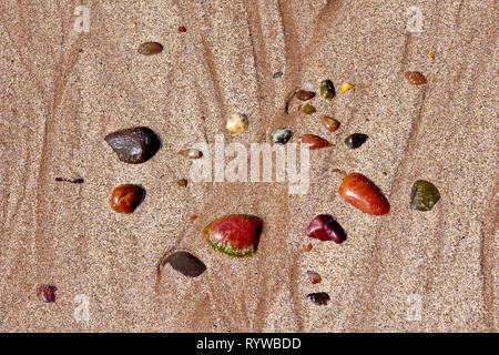 A collection of colourful scattered wet pebbles left behind on the sand after the tide goes out. Stock Photo