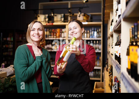 Picture of young women with bottle of wine in hands in store Stock Photo