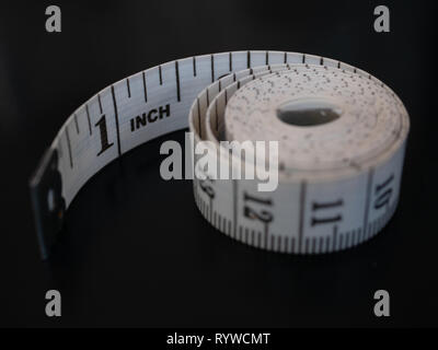 close-up tailor measuring tape isolated on black background. first one inch visible and rest curl up rolled in round coil bobbin spiral Stock Photo