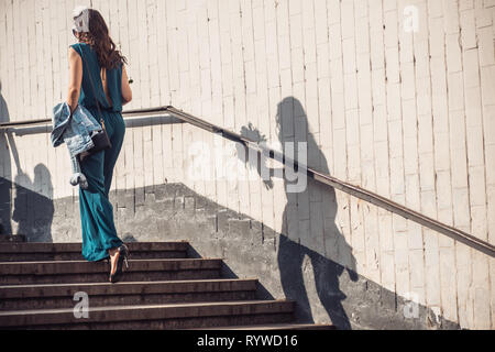 a girl in a beautiful green dress as an overalls holds flowers in her hands and goes up the steps from the underpass to the top. Frame in motion Stock Photo