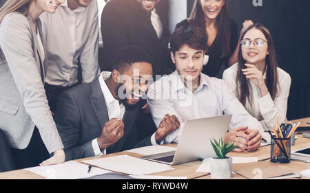Happy coworkers celebrating successful startup looking at laptop Stock Photo