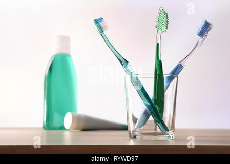 Toothbrushes in a glass cup on a wooden table and toothpaste and mouthwash in the background. Horizontal composition. Front view. Stock Photo