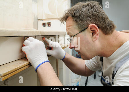 Worker is puting the piece of tile on the curved wall under a sink. Stock Photo
