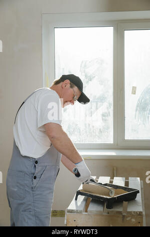 Painter is gaining paint on the roller dipping into the tray. Stock Photo