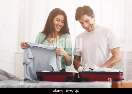 Happy couple packing clothes into suitcase, preparing for vacation Stock Photo