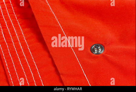 Close-up on a button of a red colored windbreaker, with a pattern created by parallel seams Stock Photo