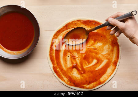 Man spreading tomato paste on pizza base Stock Photo