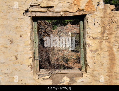 Central empty green window frame on rocky wall of abandoned house.  Through frame see barbed wires and rest of structure in ruin Stock Photo
