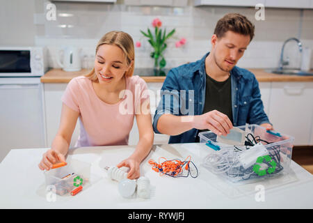Recycling, reuse, energy. Young couple sorting batteries, other electronic waste into containers with recycling symbol while sitting at kitchen Stock Photo