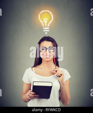 Portrait of a beautiful woman with bright light bulb above head holding a book and smiling Stock Photo