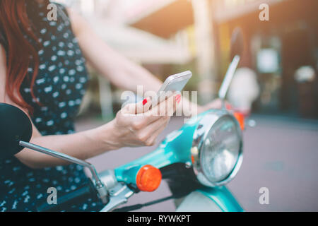 Beautiful young woman dressed casual sitting on scooter and talking on phone. Girl sitting on the bike and using Cellular smartphone Stock Photo