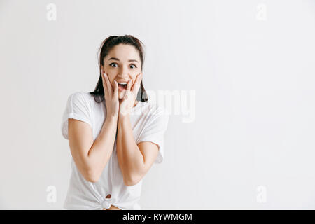 Wow. Beautiful female half-length front portrait isolated on gray studio backgroud. Young emotional surprised woman standing with open mouth. Human emotions, facial expression concept. Stock Photo