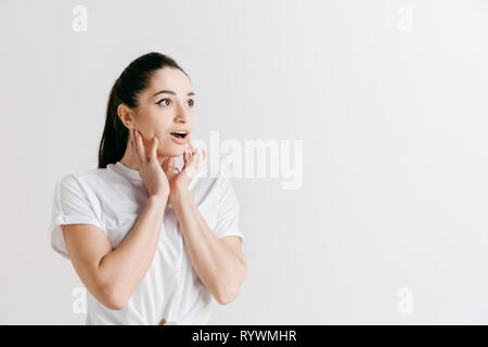 Wow. Beautiful female half-length front portrait isolated on gray studio backgroud. Young emotional surprised woman standing with open mouth. Human emotions, facial expression concept. Stock Photo