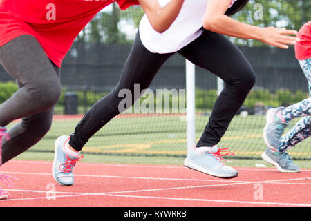 Three girls race each other sprinting at high school track and field practice outside on a red track. Stock Photo