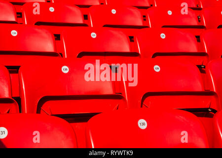Rows of numbered foldable shiny red plastic seating for fans on terraces of Main Stand at Liverpool Football Club Anfield Road Stadium, Lancashire UK. Stock Photo