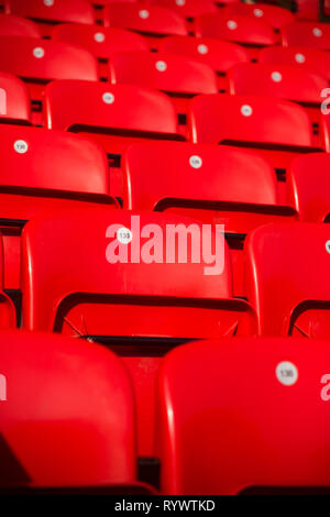 Rows of numbered foldable shiny red plastic seating for fans on terraces of Main Stand at Liverpool Football Club Anfield Road Stadium, Lancashire UK. Stock Photo