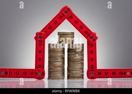 Stack Of Coins Under The House Made With Red Measuring Tape On The Desk Stock Photo