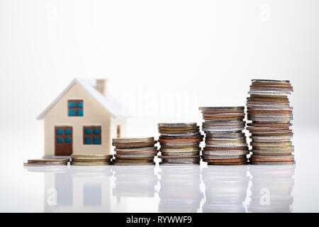 Increasing Coins Arranged In Front Of House Model Over White Desk