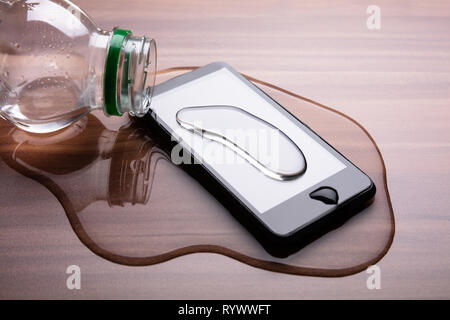 Close-up Of Spilled Water On Smart Phone Over Wooden Desk Stock Photo