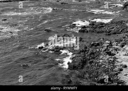 Ocean waves crashing onto rocky shoreline, black and white. Stock Photo
