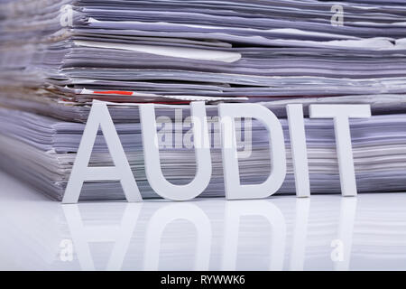 Close-up Of Audit Word And Stacked Document On Reflective Desk Stock Photo