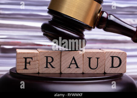 Close-up Of Wooden Gavel Striking On Wooden Block With Fraud Word Against Blurred Background Stock Photo