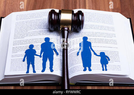 Blue Paper Cutout Of Separated Family On Open Book With Gavel Over Wooden Table Stock Photo