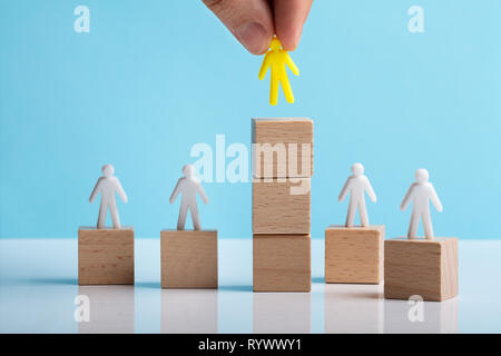 Hand Placing Human Figure Over Stacked Wooden Block On White Desk Stock Photo