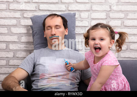 Adorable Child Painting Father's Face While He Is Sleeping On Sofa Stock Photo