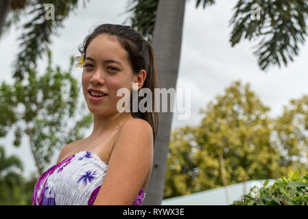 Closeup of young girl standing under tree in sundress with smile on her face Stock Photo