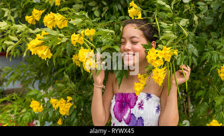 Young girl in flowered dress standing in front of flowers and smiling Stock Photo