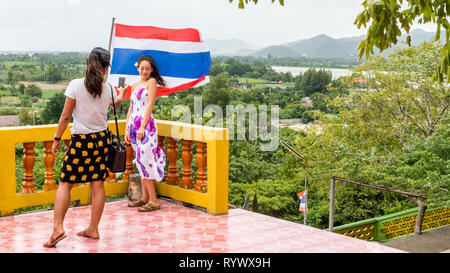Mother taking photo of smiling daughter in front of Thai flag Stock Photo