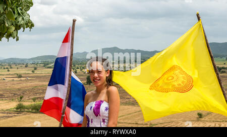 teen standing between  thai and temple flags on windy day with fields and mountains in the back ground Stock Photo